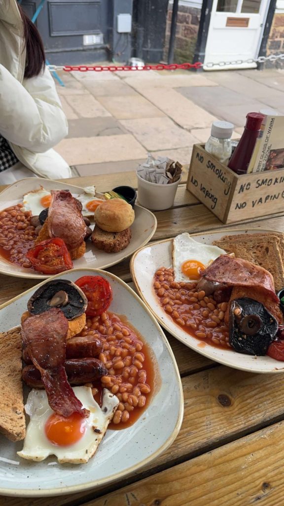 Three full English breakfast plates on an outside wooden table