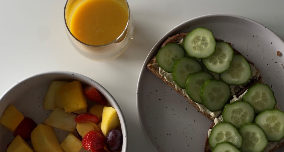 Orange juice, a bowl of fruit salad and two slices of toast with hummus and cucumber