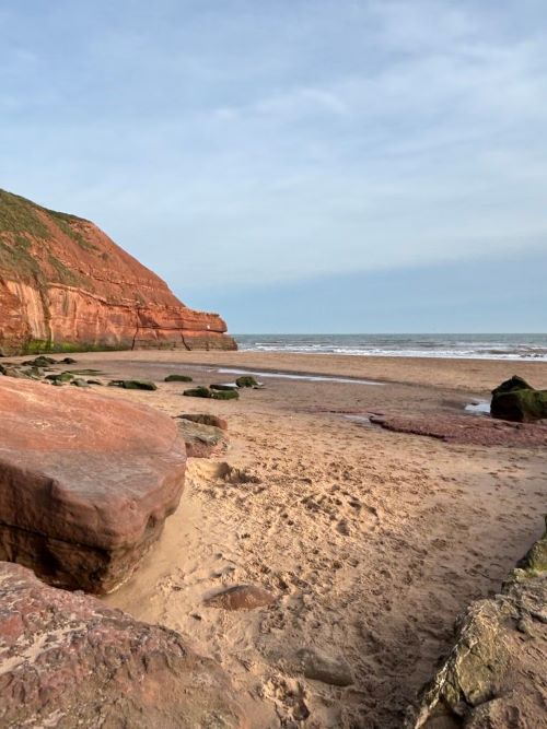 An empty beach with large, red cliffs behind