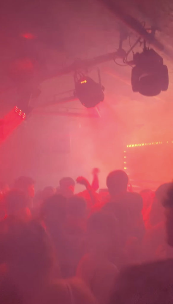 Hazy image of people dancing in a night club with their hands in the air. Hues of reds, oranges and yellows.