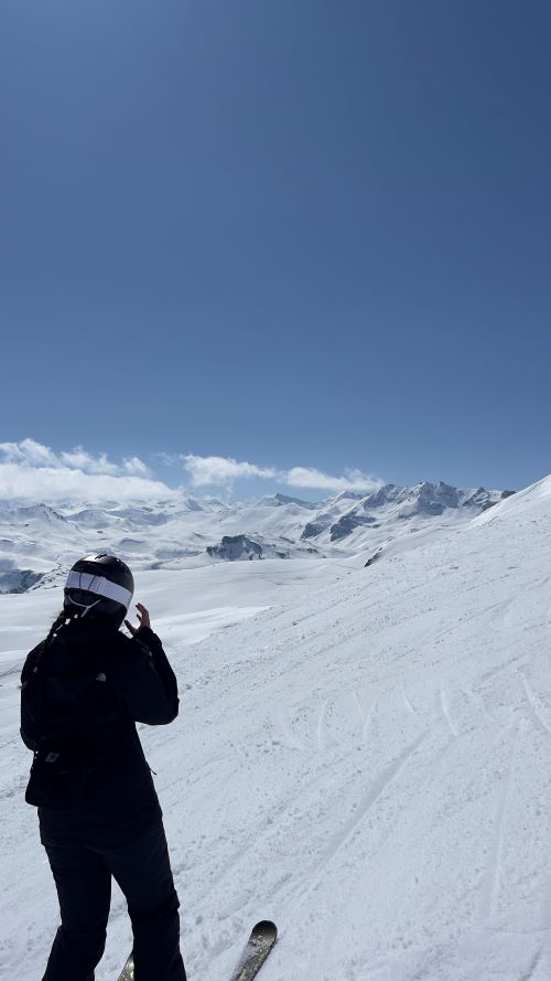 Female student wearing ski kit on an empty snowy mountain in the sunshine