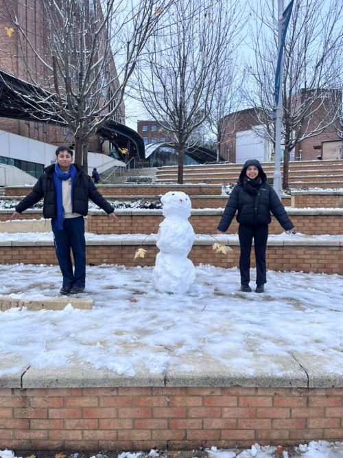 Students standing either side of a snowman outside the Forum of Streatham Campus