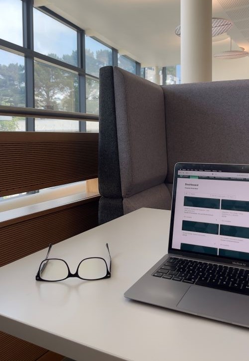 A laptop and a pair of glasses on a study desk by a window