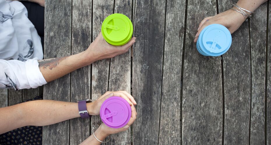 Hands holding reusable cups on a wooden picnic bench