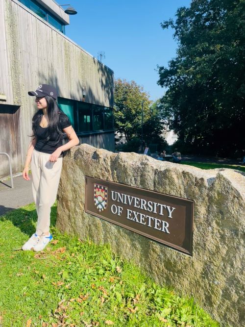 Student standing by a University of Exeter sign on a rock