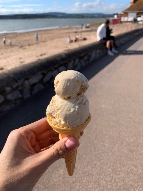 Hand holding an ice cream in front of a sunny beach