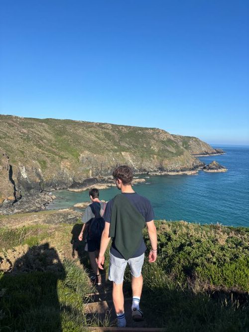 Students walking on a cliff path next to a bright blue sea on a sunny day