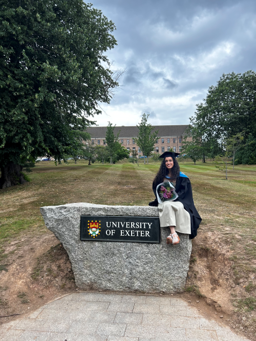 A student in graduation robes sat on the University of Exeter rock