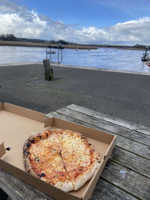 Takeaway pizza on a wooden picnic bench in front of Topsham estuary