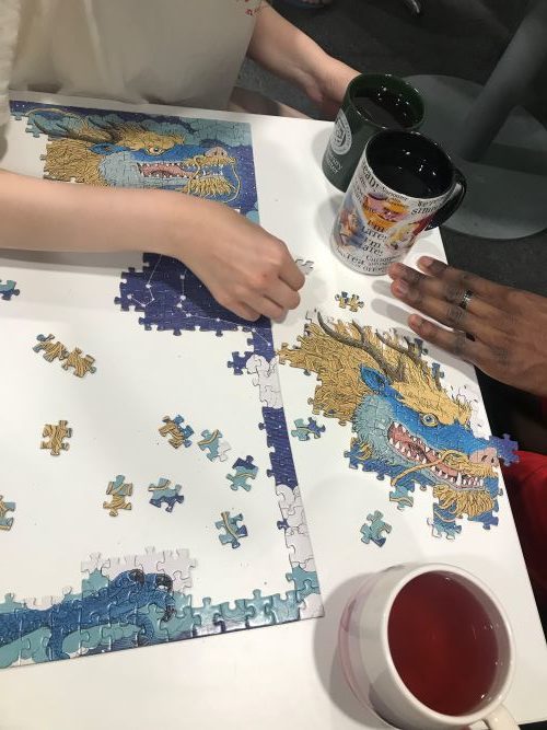 A half-finished jigsaw and several cups of tea on a table