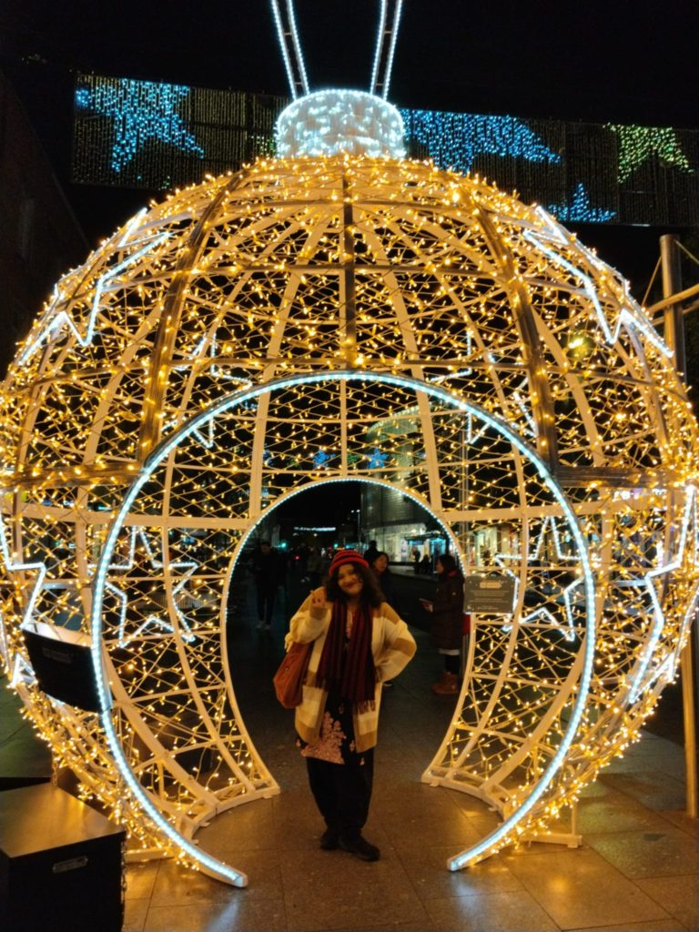 The writer of the blog standing in a giant Christmas bauble with lights on in Exeter