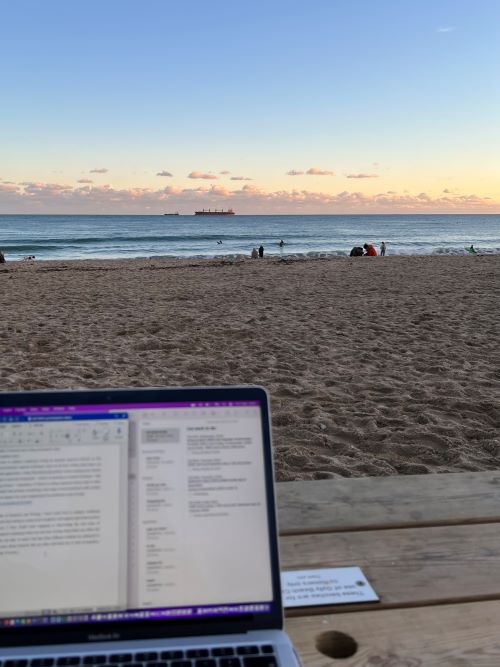 Laptop open on a picnic bench at the beach at sunset