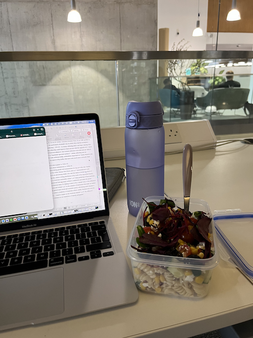 A healthy homemade pasta salad next to a laptop on campus