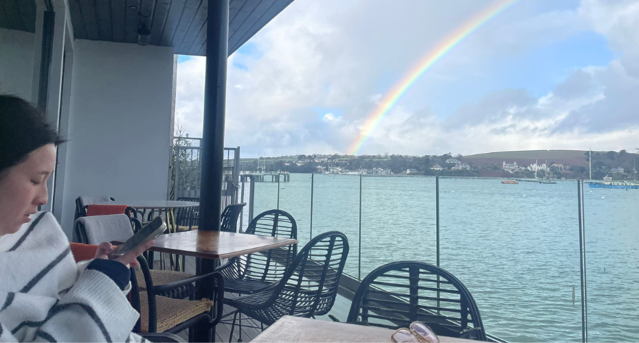 Outside cafe seating overlooking an estuary and a rainbow