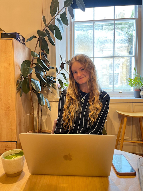 A photo of me sitting with my laptop and a matcha in The Poly cafe, with plants and a window view