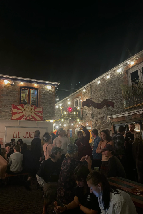 Outside a pub filled with people. Dark outside with fairy lighting.