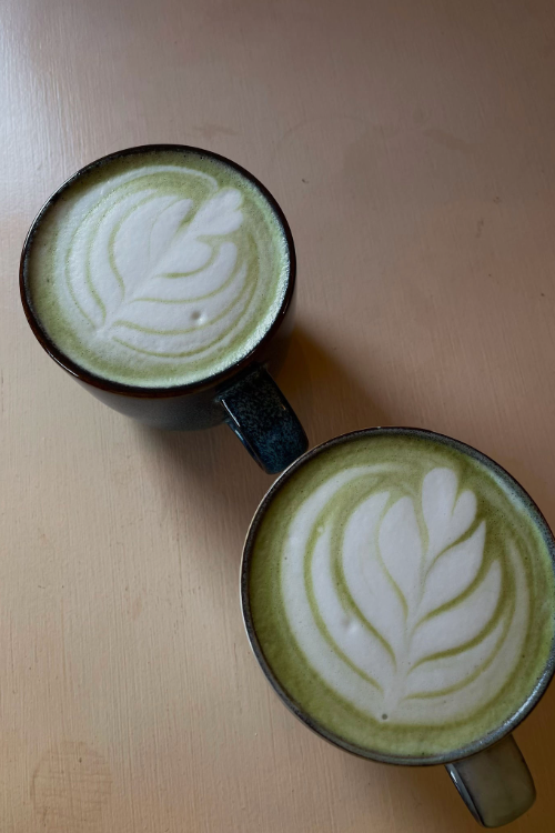 Two mugs of matcha latte, with heart design on the lattes.