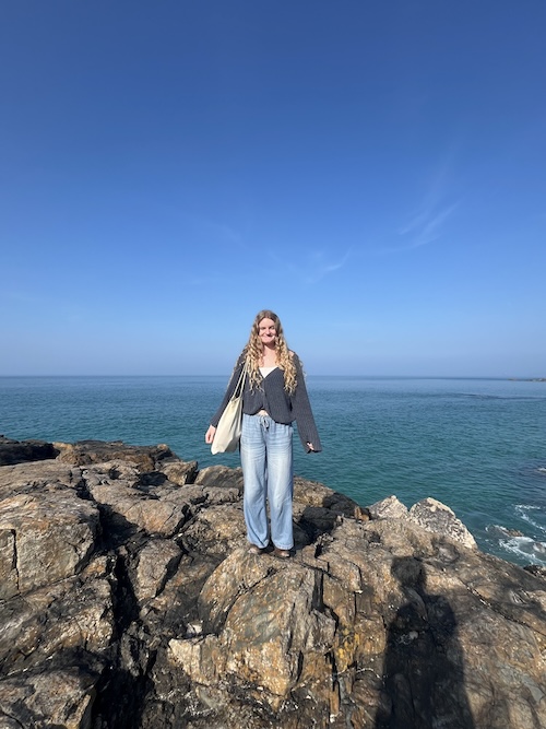 A photo of me smiling on a rock next to the sea in St Ives