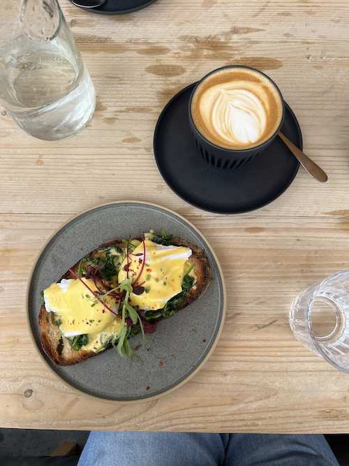 A light picture of a wooden table with a flat white coffee next to a plate of nicely garnished eggs benedict