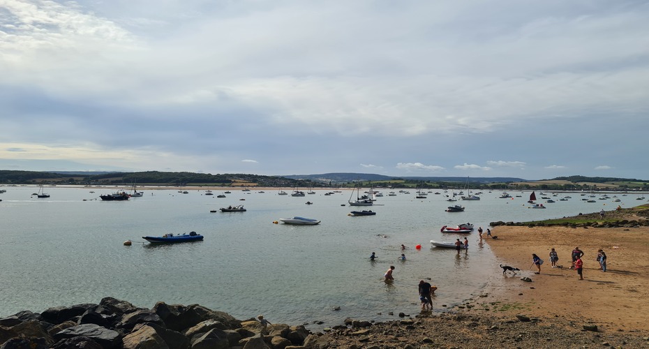 Exmouth Beach, showing many small boats in the water and people at the shoreline.