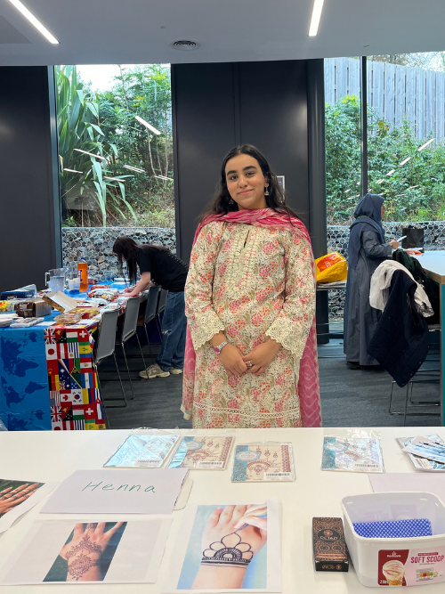 Reeham wearing traditional attire standing behind a table set up for the henna stall.