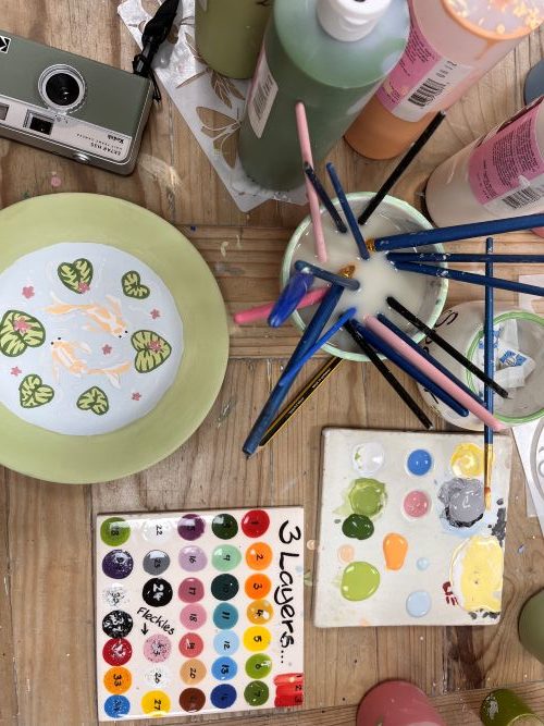 Pottery painting scene, with a painted plate, paintrush cup and paint colours.