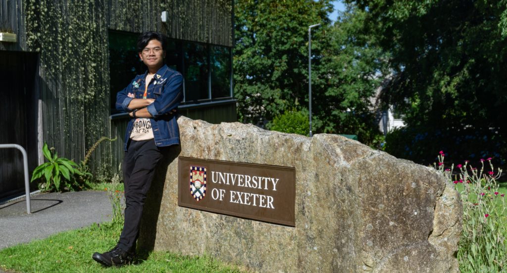 A person standing next to a stone monument with the University of Exeter logo
