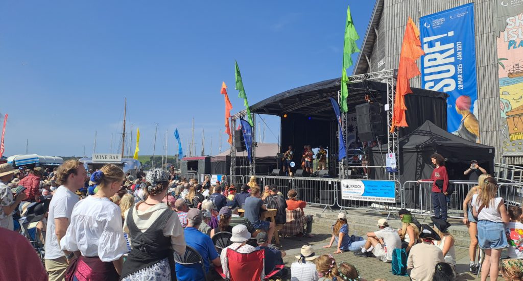 A large crowd of people gathered in front of an outdoor festival stage during a performance.