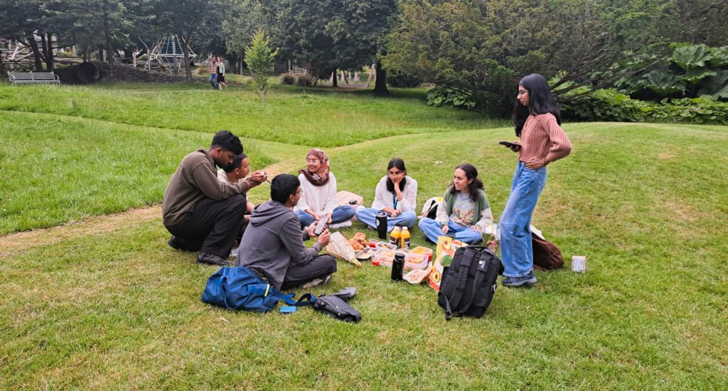 A group of people sitting on the grass with food and drinks