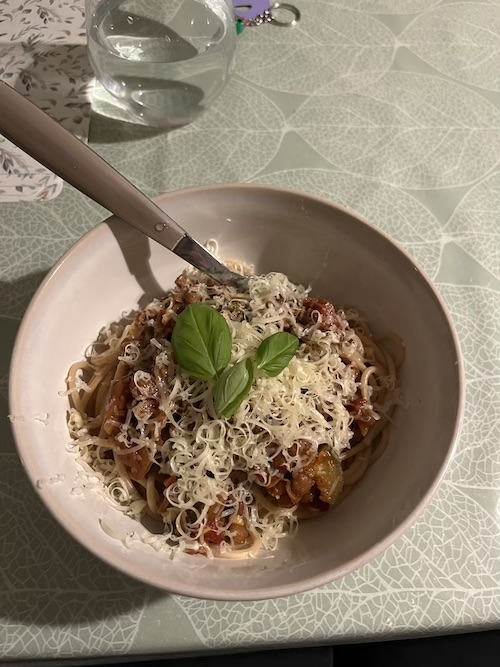 A bowl of lentil spaghetti bolognese with cheese and basil