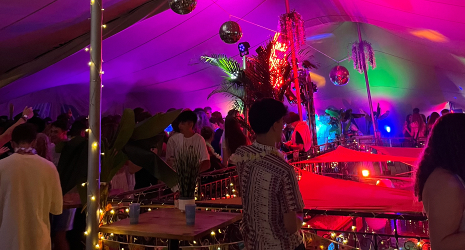 A outdoor marquee tent with multicoloured lights, disco balls and fairy lights. Students dancing.