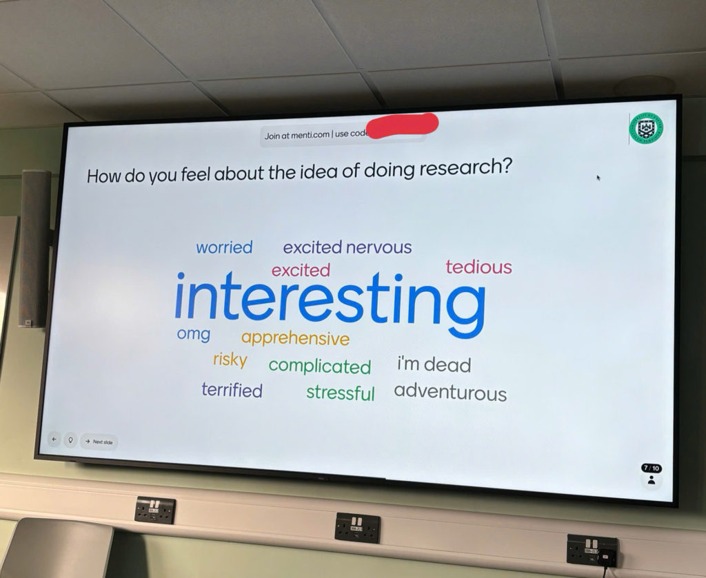 Photo of a powerpoint screen with a Menti.com discussion question of 'How do you feel about the idea of doing research', with a variety of responses