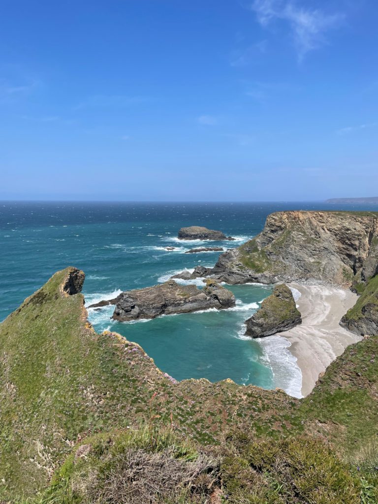View from cliffs down onto a beach with large stacks in the water.