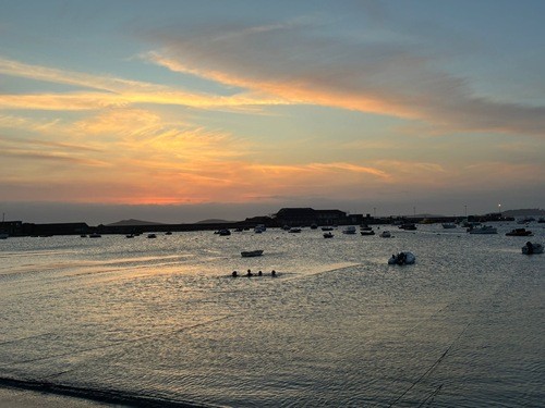Sunset over the harbour with four people swimming in the sea.