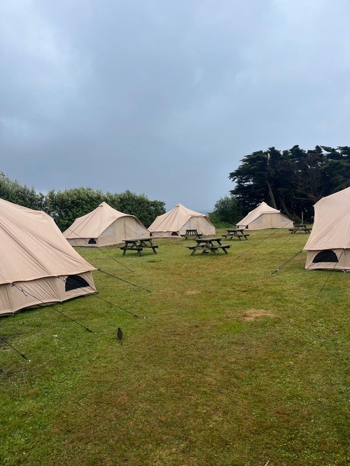 Five large brown tents in a circle with some picnic benches in the centre.