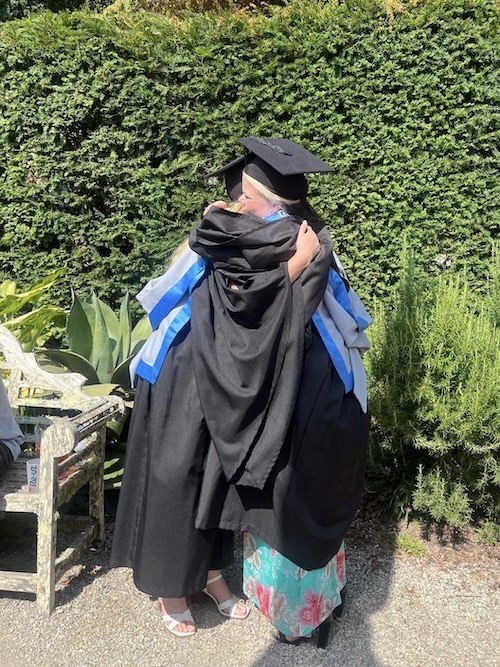 A candid photo of two women in graduation gowns and hats hugging